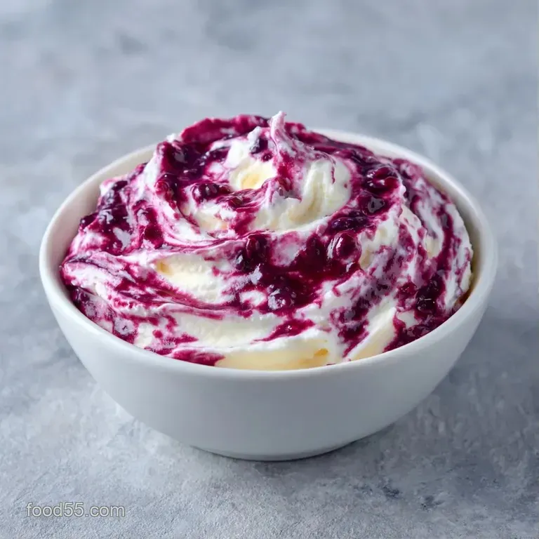 A sophisticated glass dish filled with velvety white cream and topped with a cluster of ripe purple berries.