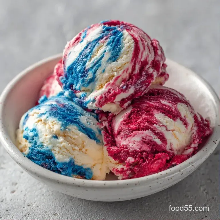 Three colorful scoops of red, white, and blue frozen dessert in a glass goblet garnished with a fresh blueberry.