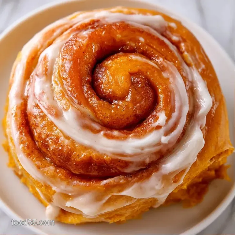 Spiral-shaped orange pastry on a white plate, drizzled with a glossy white glaze and a sprinkle of cinnamon.